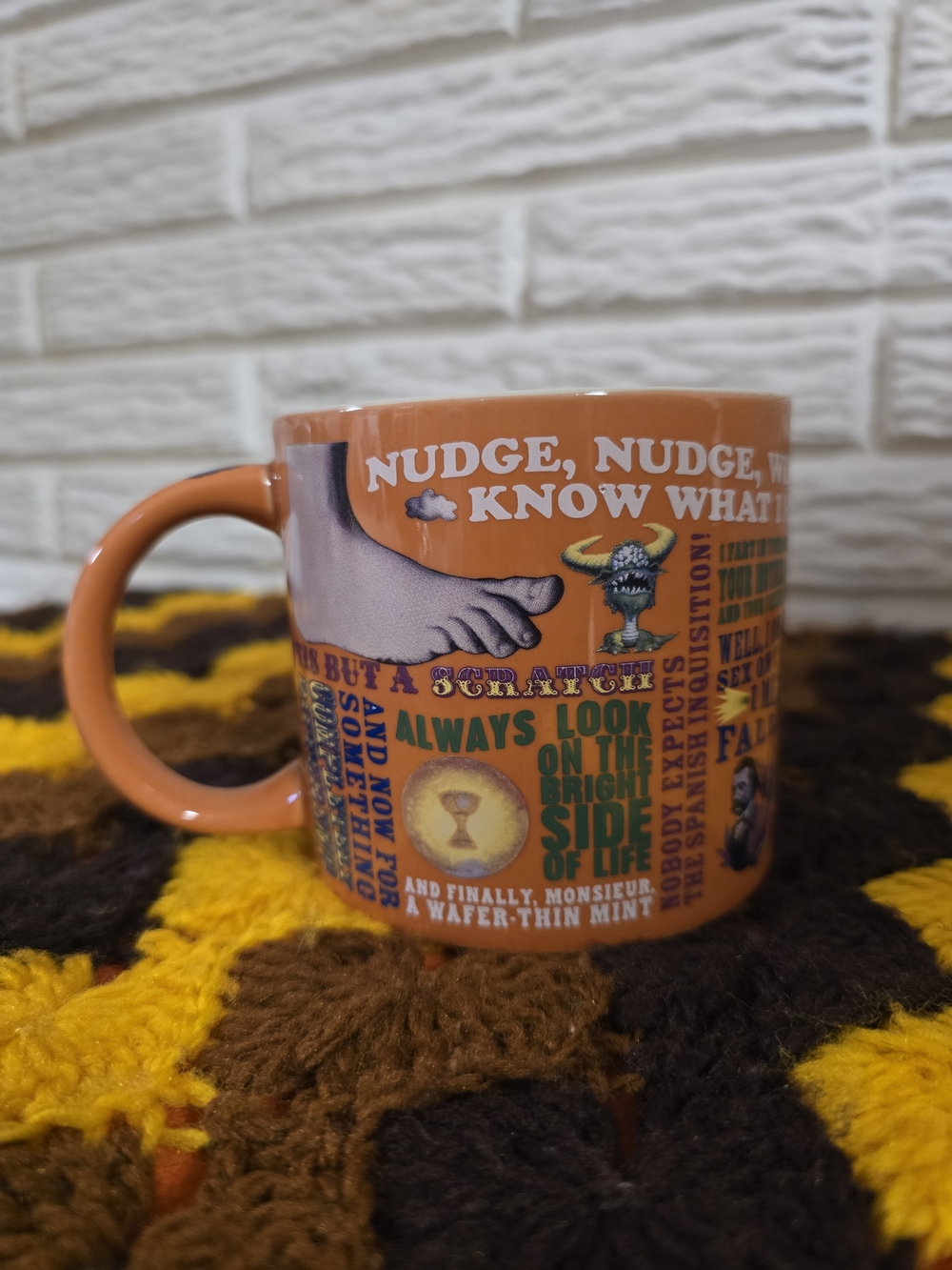 orange coffee mug features classic quotes and imagery from Monty Python sketches